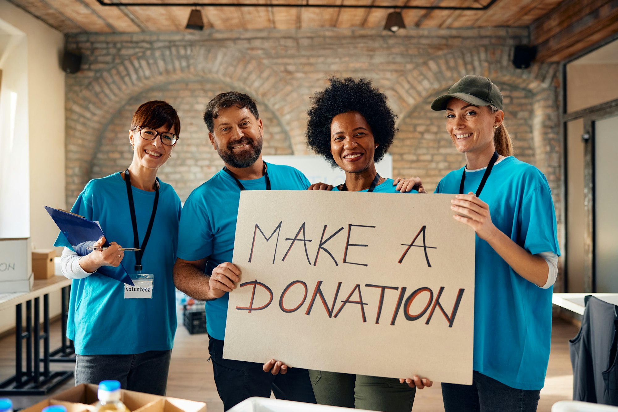 Multiracial group of happy volunteers with 'make a donation' placard looking at camera.